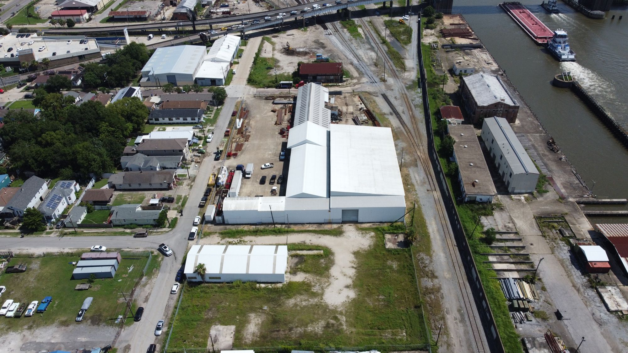 Aerial view of the Japonica Works campus: the small white building at 1333 Japonica Street in front, the large white warehouse at 1435 Japonica Street behind it, with the railroad, the Industrial Canal and the Claiborne Avenue bridge beyond.